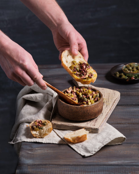 意大利菜。橄榄和山柑酱。开胃酒。木桌上放着橄榄油和意大利脆皮面包。意大利菜。厨师准备意式烤面包。食物照片中的男人的手。图片下载