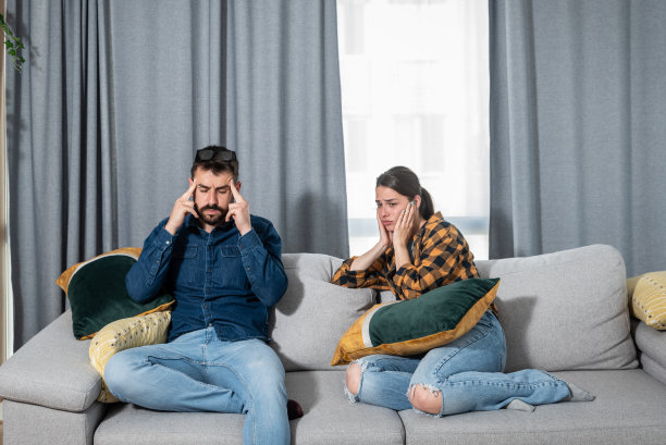 一对年轻夫妇坐在公寓的沙发上，用手捂住耳朵，而楼上的邻居正在举行派对，大声播放音乐，或者在装修公寓图片下载