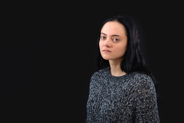 年轻女子的肖像与长黑发穿着灰色针织毛衣在黑色背景图片下载