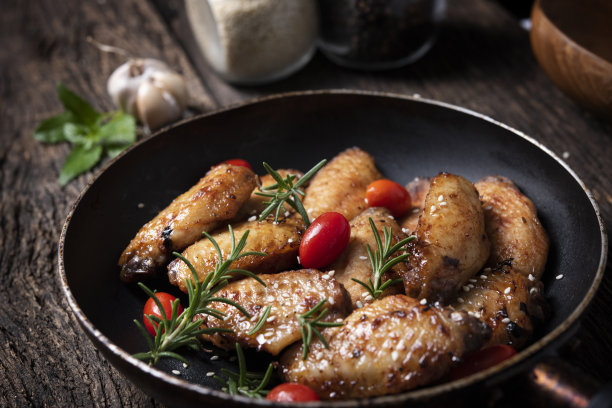 在平底锅中加入不同调味料的烤鸡翅。黑色背景图片下载