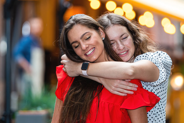 快乐的相遇两个朋友拥抱在街上，散焦的灯光背景图片下载