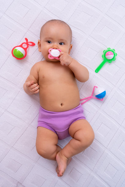 一个嘴里叼着奶嘴的新生婴儿躺在白色针织毯子上，垂直照片图片下载