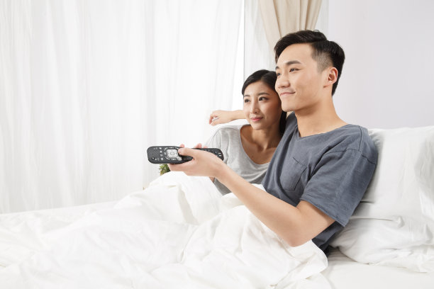 青年情侣坐着床上看电视图片下载