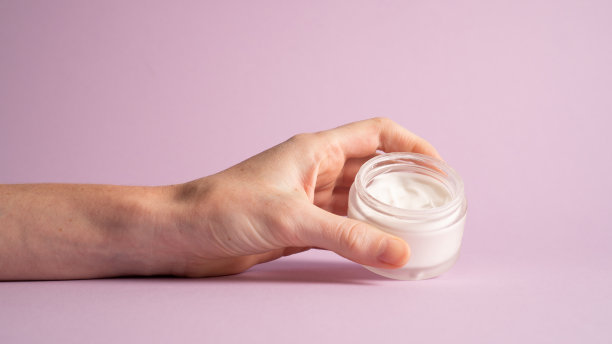 奶油色的罐子在黄色的背景上孤立。一个女人拿着一个装满化妆品的罐子图片下载