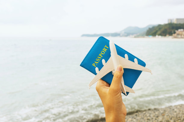 女人手拿护照和玩具飞机在海上背景，旅行概念图片下载