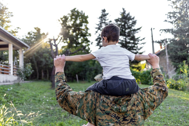 年轻的军人把儿子抱在肩膀上，双臂高举在空中，望向别处。图片下载