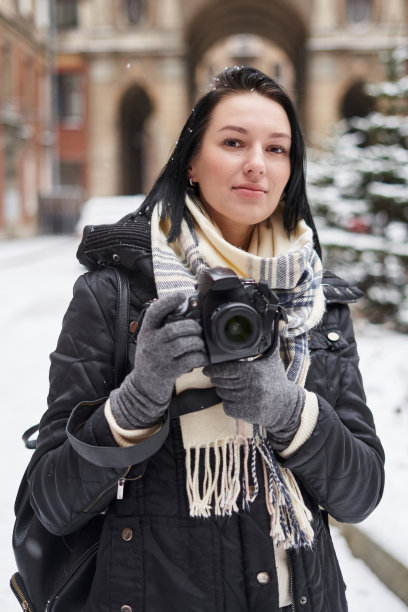 一个年轻的女人在冬天拿着相机走在街上。图片下载
