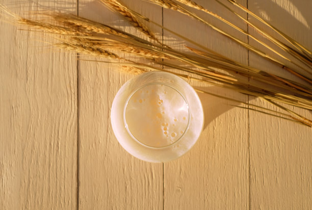 一杯新鲜的小麦啤酒和木桌上金色的成熟小麦穗，俯视图图片下载