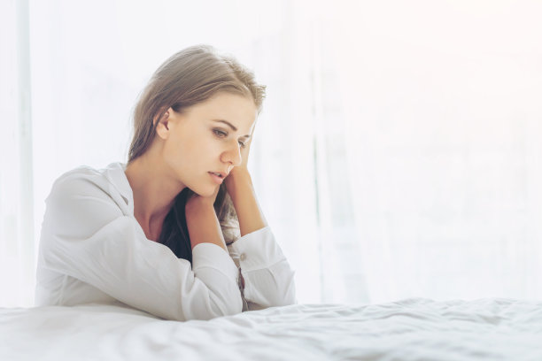 一个美丽的女人的肖像可爱的女孩独自坐在床边感到悲伤在白色的早晨卧室图片下载