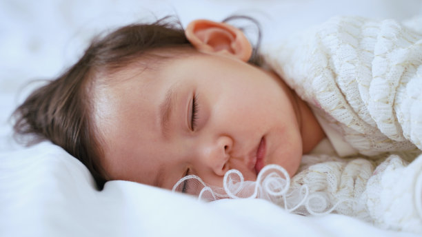 近距离拍摄可爱的小女孩睡在白色的床上，1岁，柔焦照片图片下载