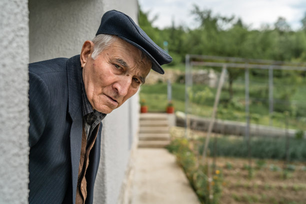 在欧洲巴尔干村的一个农场里，一位年老的白种人退休老人站在自己家的门口，看着旁边真实的人的概念图片下载