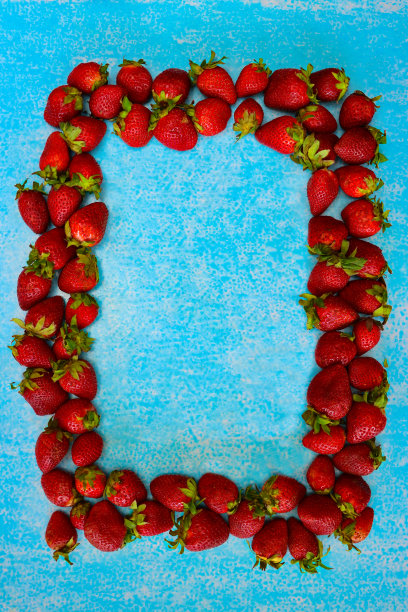 整个特写图像，新鲜的红色草莓与绿色的叶子框架，蓝绿色的背景，复制空间，升高的视野图片下载