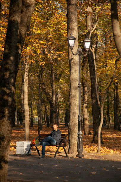 在秋天的城市公园里，一个悲伤的人拿着一束花坐在长椅上，等待了很长时间。一个失败的日期图片下载