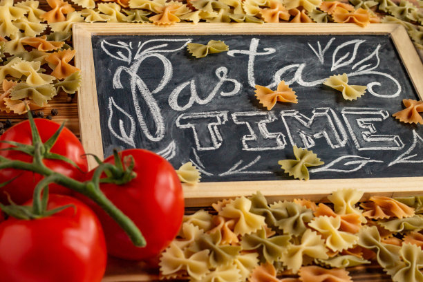 木制桌面上的粉笔板上写着“意大利面时间”，上面还有生的farfalle、新鲜的番茄和黑胡椒图片下载