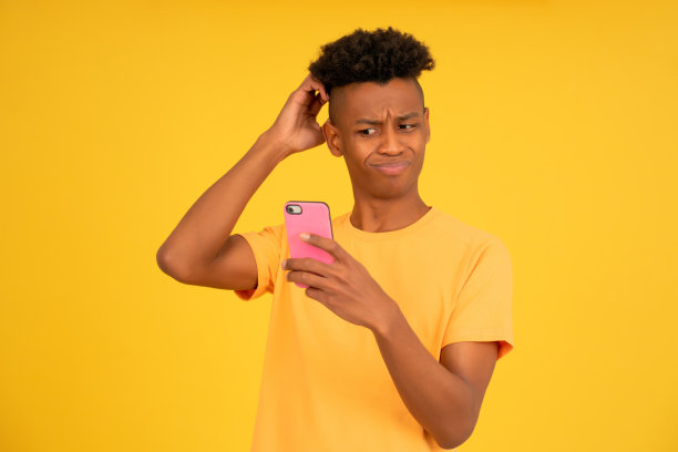 年轻的非洲头男子在使用手机时看起来很困惑。图片下载