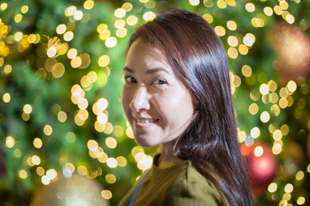 美丽的女人微笑着，圣诞树后面亮着五颜六色的霓虹灯图片下载