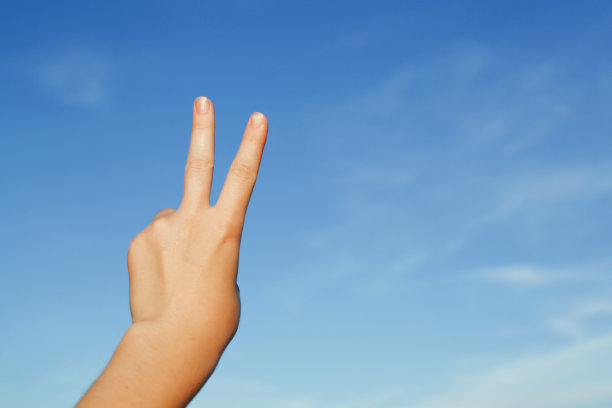 一只手在蓝天的背景下，显示胜利或和平的标志，是用食指和中指向上显示的拉丁字母“V”的形式，复制空间。图片下载