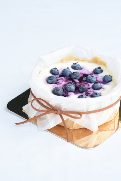 蓝莓芝士蛋糕放在金色纸盒里，用白纸包裹，用棕色细绳系一个蝴蝶结，白色背景上。图片下载