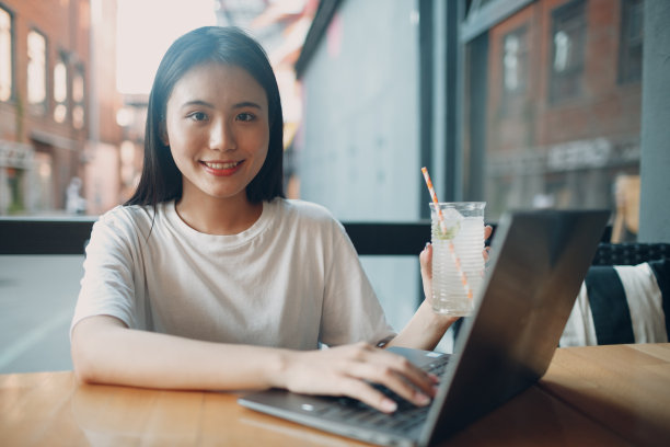 亚洲年轻女子喝柠檬汽水和使用笔记本电脑在户外咖啡馆图片下载