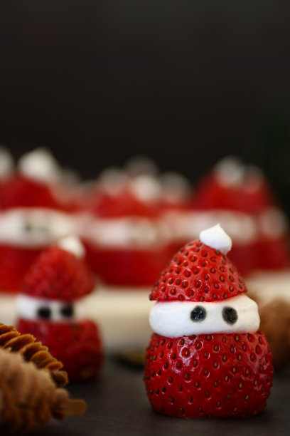 圣诞主题派对食物创意特写图片，大理石蛋糕架子上的草莓圣诞老人，圣诞老人草莓和鲜奶油，黑色背景，聚焦前景图片下载