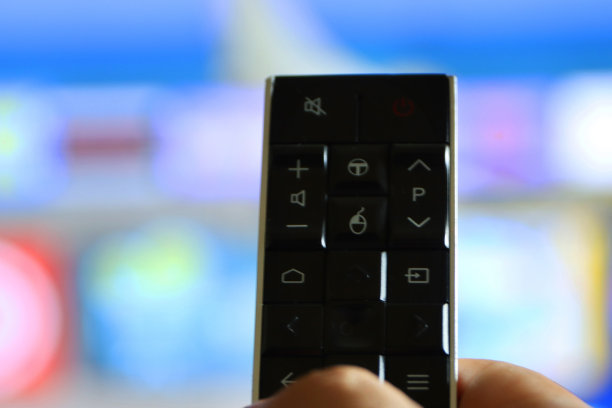 特写图片显示一个无法辨认的人的手拿着电视遥控器，指着电视屏幕，从一排排的智能电视屏幕应用程序图标和背景切换频道图片下载