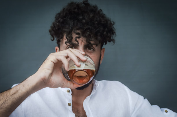 一个留着胡子和卷发的年轻人在喝啤酒图片下载