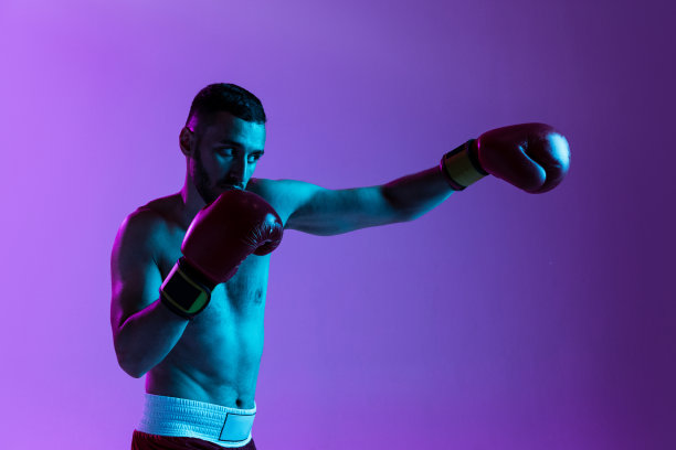 一个职业拳击手的裁剪肖像在红色制服训练孤立的紫色背景在霓虹灯。直拳移动图片下载