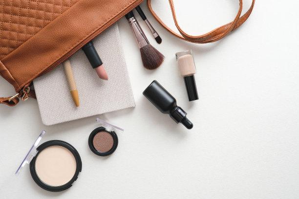 女包化妆化妆品和纸笔记本在白色的书桌桌上。平铺，俯视图。图片下载