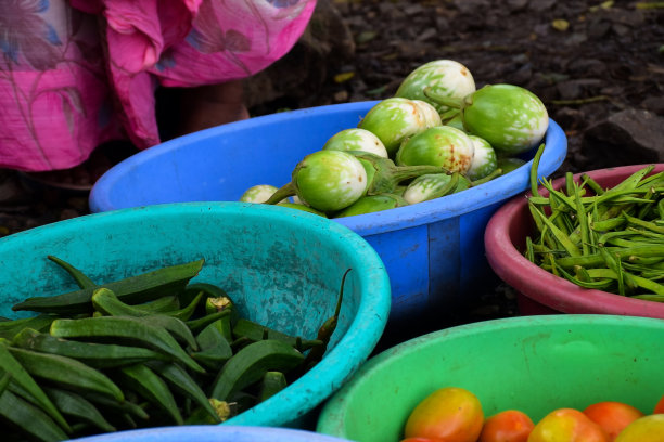 在印度马哈拉施特拉邦科尔哈普尔的当地蔬菜市场出售的塑料容器或圆形塑料篮子中的新鲜集群豆类，白茄子，秋葵和番茄的库存照片。图片下载