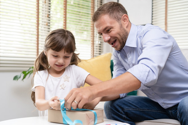 父亲节那天，可爱的女儿和爸爸帮她打开礼品盒。快乐的家庭节日打开礼盒团聚。图片下载