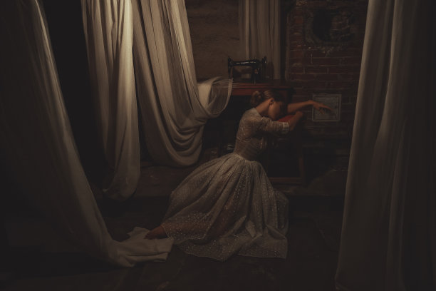 在挂满白色窗帘的旧车间里，年轻的疲惫的女裁缝在她的古董缝纫机旁休息图片下载