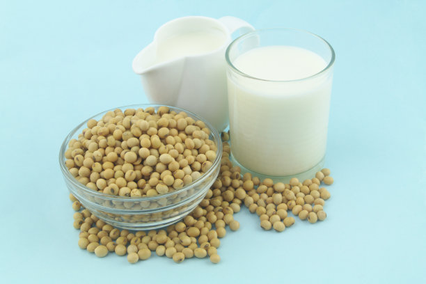 豆浆装在白色的罐子和玻璃里，蓝色的背景是大豆图片下载