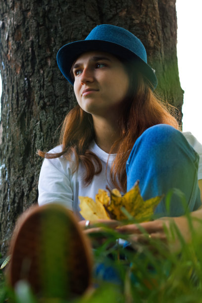 离焦的肖像，一个浪漫的年轻女子棕色头发戴着一顶帽子在户外。女手捧枯黄的枯叶。你好,秋天。妇女坐在秋天树干树。10月的心情。的焦点图片下载