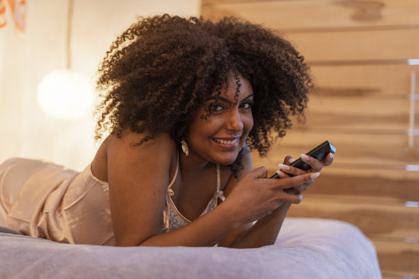 一个年轻女子的肖像在她的公寓里，穿着睡衣躺在床上看电视图片下载