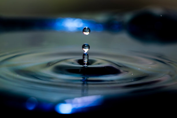 高速照片的水滴与波纹在平静的水在蓝色。使用选择性的焦点。图片下载