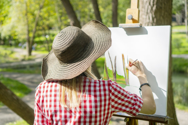 开朗的女艺术家在平原上作画。她在公园的帆布上画了一幅油画。她的画布放在画架上。女孩手里拿着画笔和调色板。创造性的情绪。图片下载