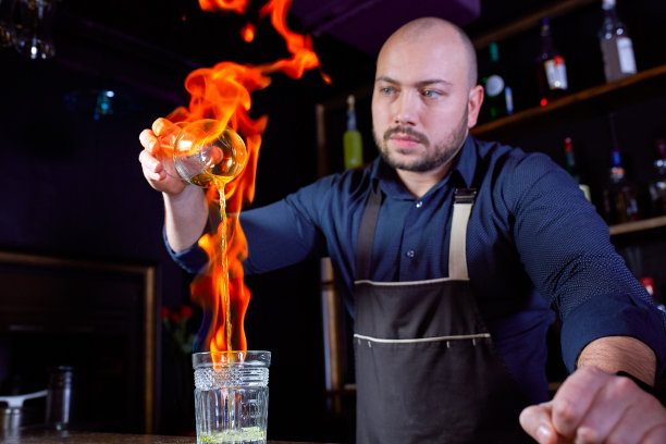 酒吧里火爆的表演。调酒师调制热酒精鸡尾酒，点燃吧台。酒保准备了烈性鸡尾酒。火在酒吧图片下载