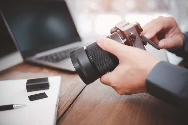 一名商人手拿相机，在桌上的记忆型笔记本电脑上查看工作中使用的照片图片下载