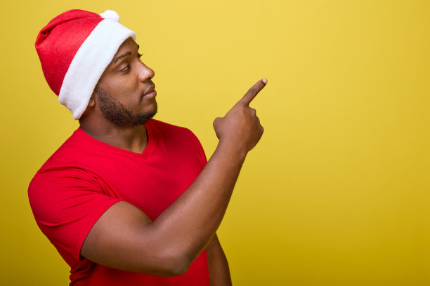 一个戴着圣诞老人帽子的黑人的肖像，他的食指指向黄色的背景图片下载
