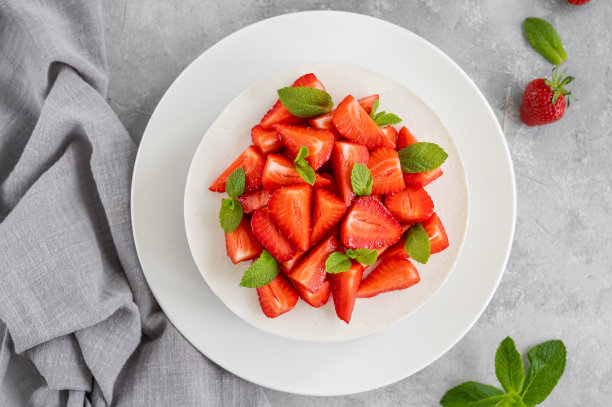 没有烤芝士蛋糕，上面有新鲜的草莓和薄荷，白色的盘子，灰色的混凝土背景。副本的空间。图片下载