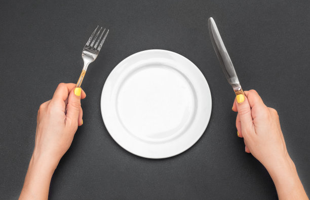 女人的手拿着刀叉在黑色的桌子上放着空盘子。图片下载