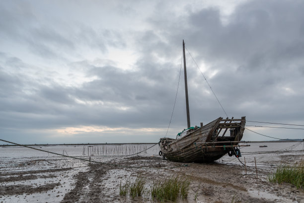 在清晨日出前的浅水区，乌云密布，海滩上有许多渔船图片下载