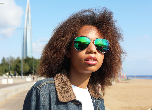 一个夏天，年轻的非洲女人穿着牛仔夹克，戴着太阳镜，坐在沙滩上休息图片下载