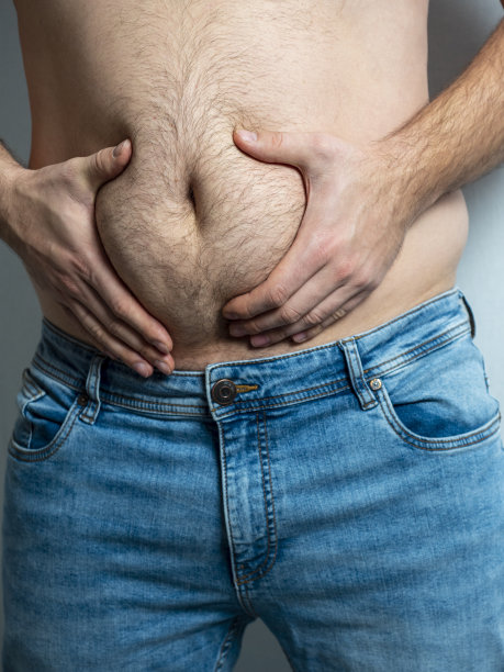 穿牛仔裤的男人挤压着他毛茸茸、松弛的胖肚子。营养不良的概念。身体积极的。自我接纳、垂直照片图片下载