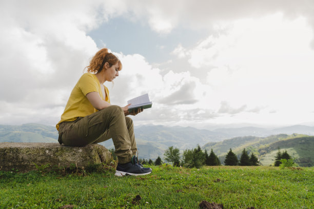 穿着黄色t恤的白人女性在森林里看书图片下载