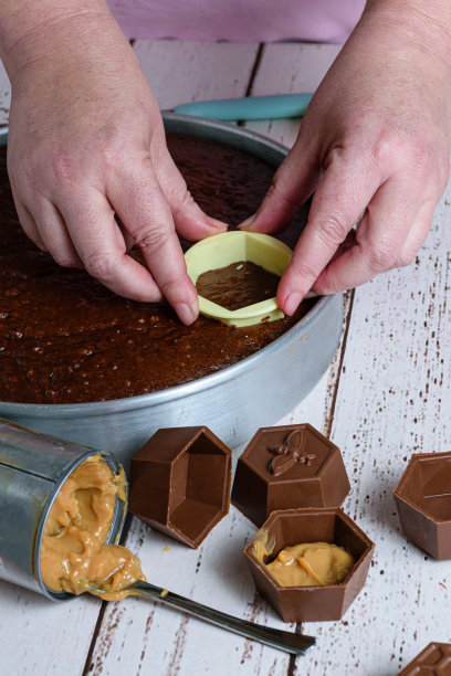 糖果师正在切一块巴西蜂蜜蛋糕，将其放入装满牛奶甜酒的巧克力模具中(垂直照片)。图片下载