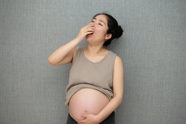 一个年轻的亚洲孕妇在墙前打哈欠图片下载