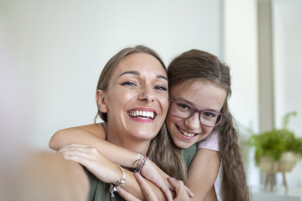 小女儿年轻的母亲面对网络摄像头近距离观察。可爱的小女孩用智能手机和姐姐一起玩自拍，视频博主记录新的视频博客，享受有趣的活动概念图片下载