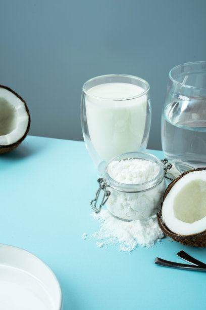 椰子产品。打开椰子，肉切成两半，椰子粉放在玻璃瓶里，蓝色背景上种上牛奶。等角投影。副本的空间。概念替代牛奶，素食图片下载
