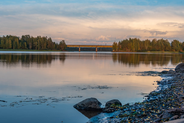 落日映照下的河流和森林。云在水中的倒影。城郊的公路桥穿过这条河。图片下载